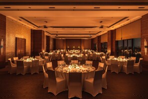 Un salón de banquetes con mesas redondas dispuestas para cenar, con un arreglo floral central y velas.