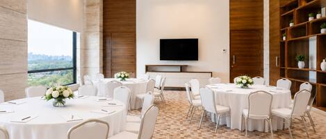 A conference room with round tables, white chairs, and a flat-screen TV on the wall.