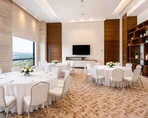 Un salón de conferencias con mesas redondas, sillas blancas y un televisor de pantalla plana en la pared.