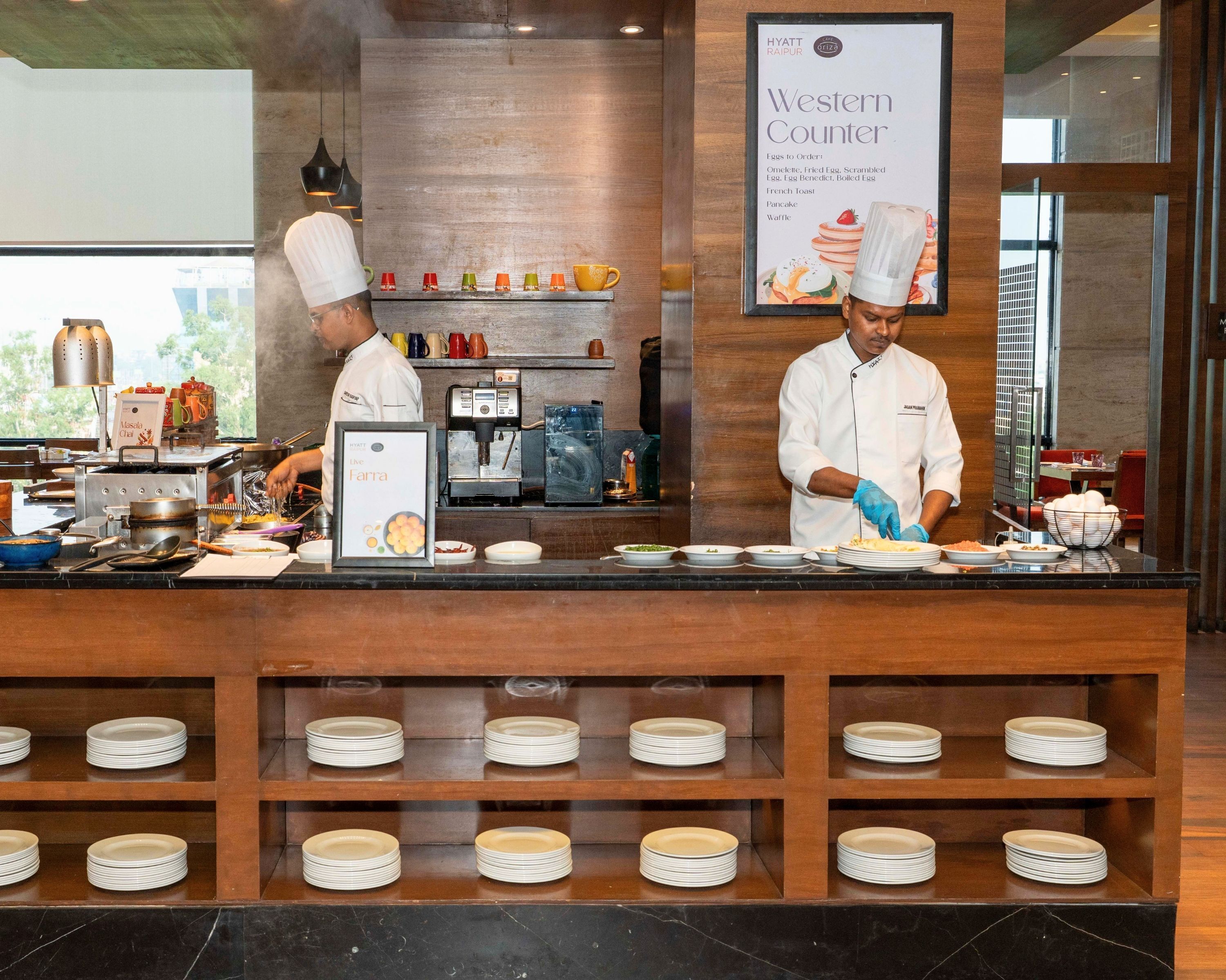 A hotel kitchen with chefs preparing food, a menu board, and a coffee machine.