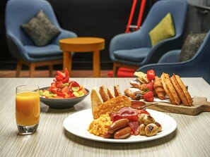 A breakfast setting with a fruit salad, toast, scrambled eggs, sausages, and a glass of orange juice on a table. - ibis Adelaide (Adelaide)