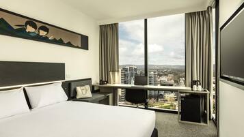 Habitación de hotel con cama, escritorio y ventana grande con vista a la ciudad.
