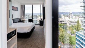 Une chambre d’hôtel moderne, dotée d’un grand lit, d’un bureau et offrant une vue sur le paysage urbain.