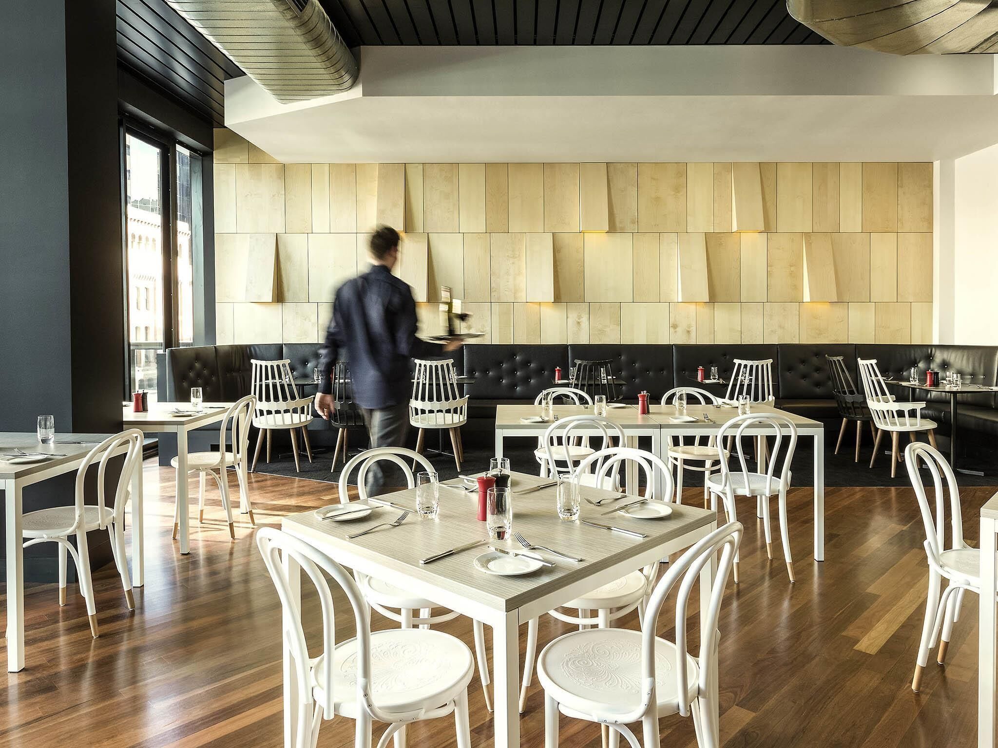 A modern restaurant interior with white chairs and tables, a black leather booth, and a person serving.