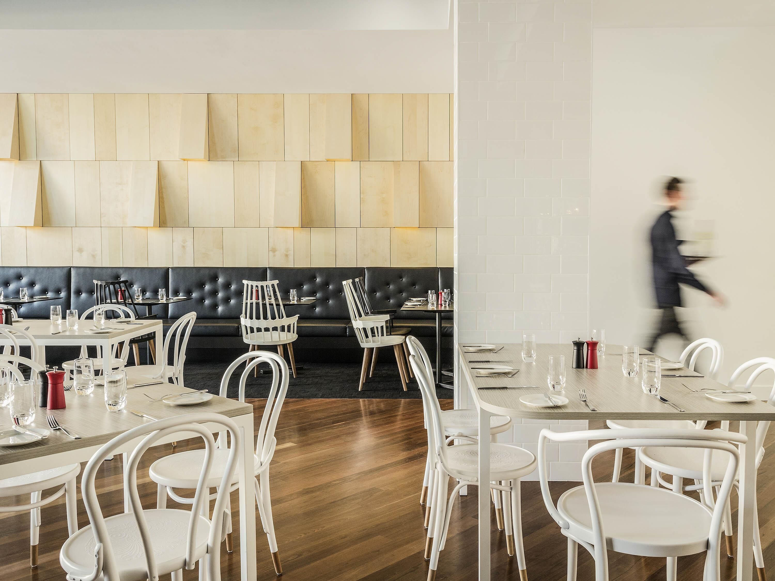Un interior de restaurante moderno con mobiliario blanco, un banco acolchado negro y suelo de madera.
