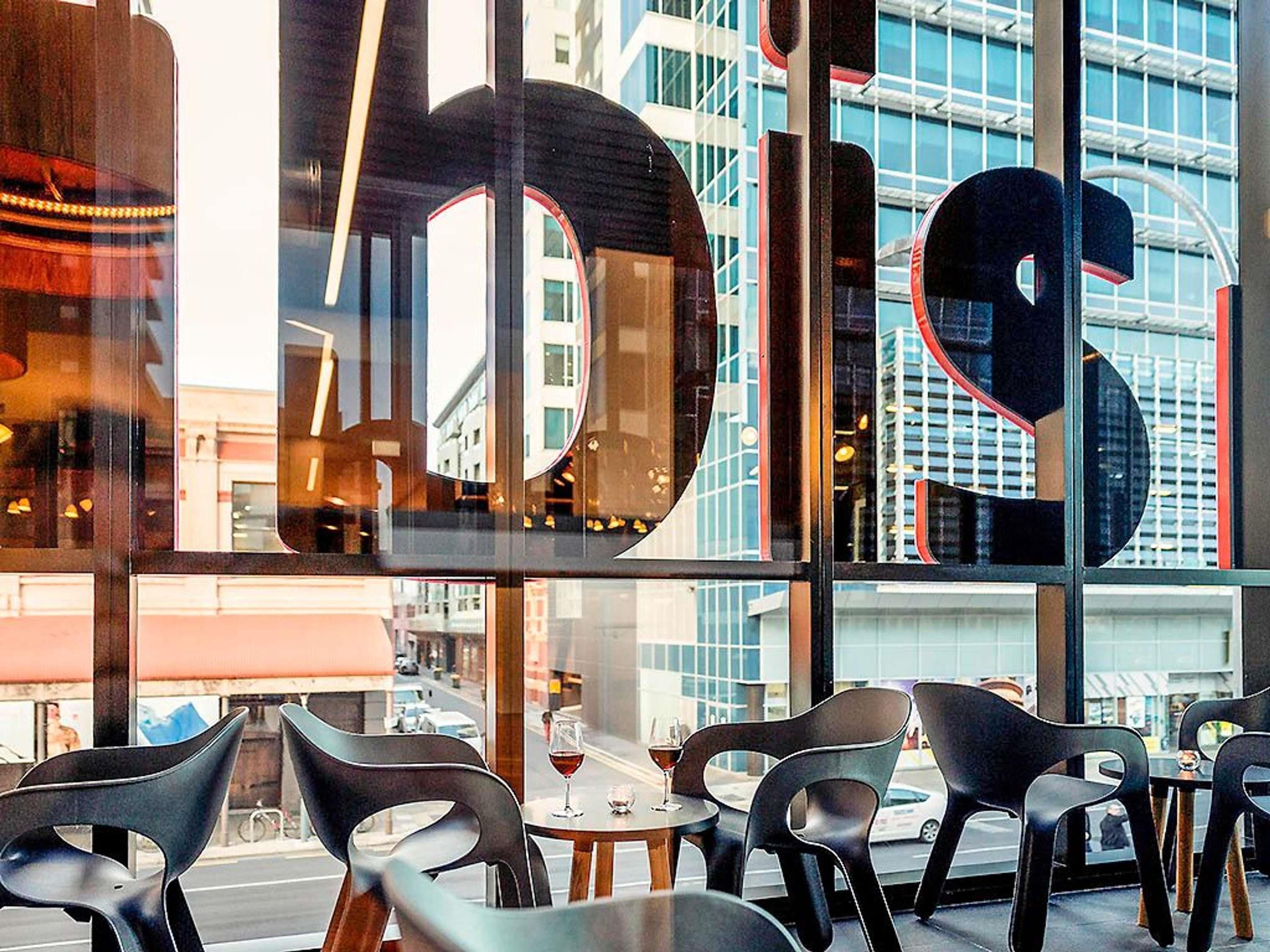 A modern interior with large windows, black chairs, and a table with a glass of red wine.