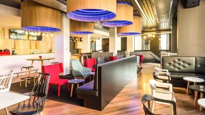 Un restaurant moderne avec de hauts plafonds en bois, des suspensions bleues et un mélange de sièges rouges et noirs.