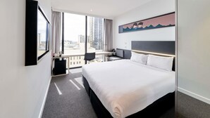 A hotel room with a large bed, a desk, a chair, a TV, and a city view. - ibis Adelaide (Adelaide)