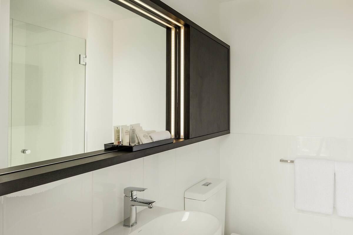 A modern bathroom with a large mirror, a chrome faucet, and a white toilet.