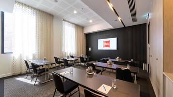 A conference room with a large screen displaying the ibis logo, multiple tables with chairs, and a patterned carpet.