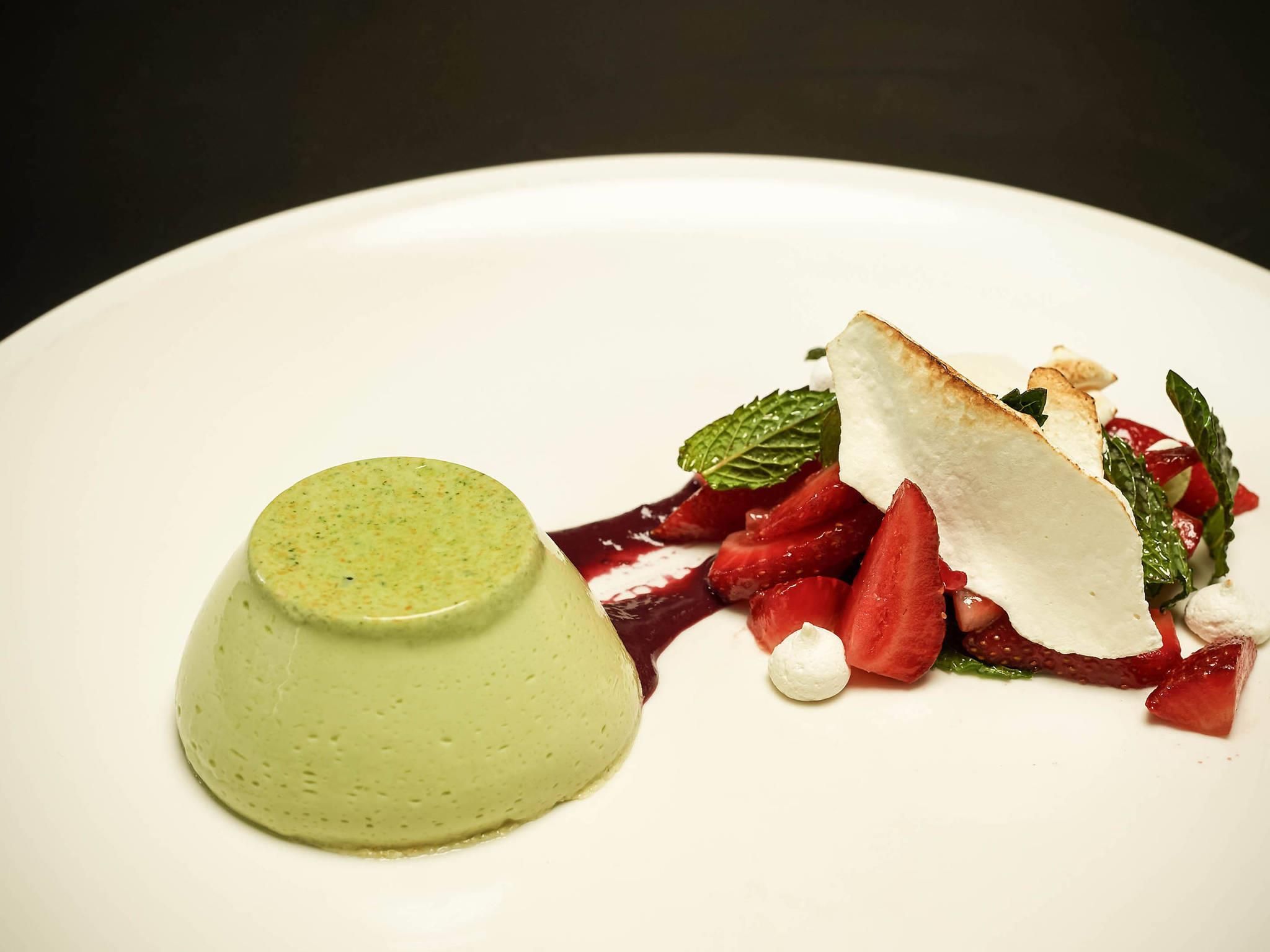 Un dessert avec une portion en forme de dôme vert et une tranche blanche, le tout présenté sur une assiette blanche.