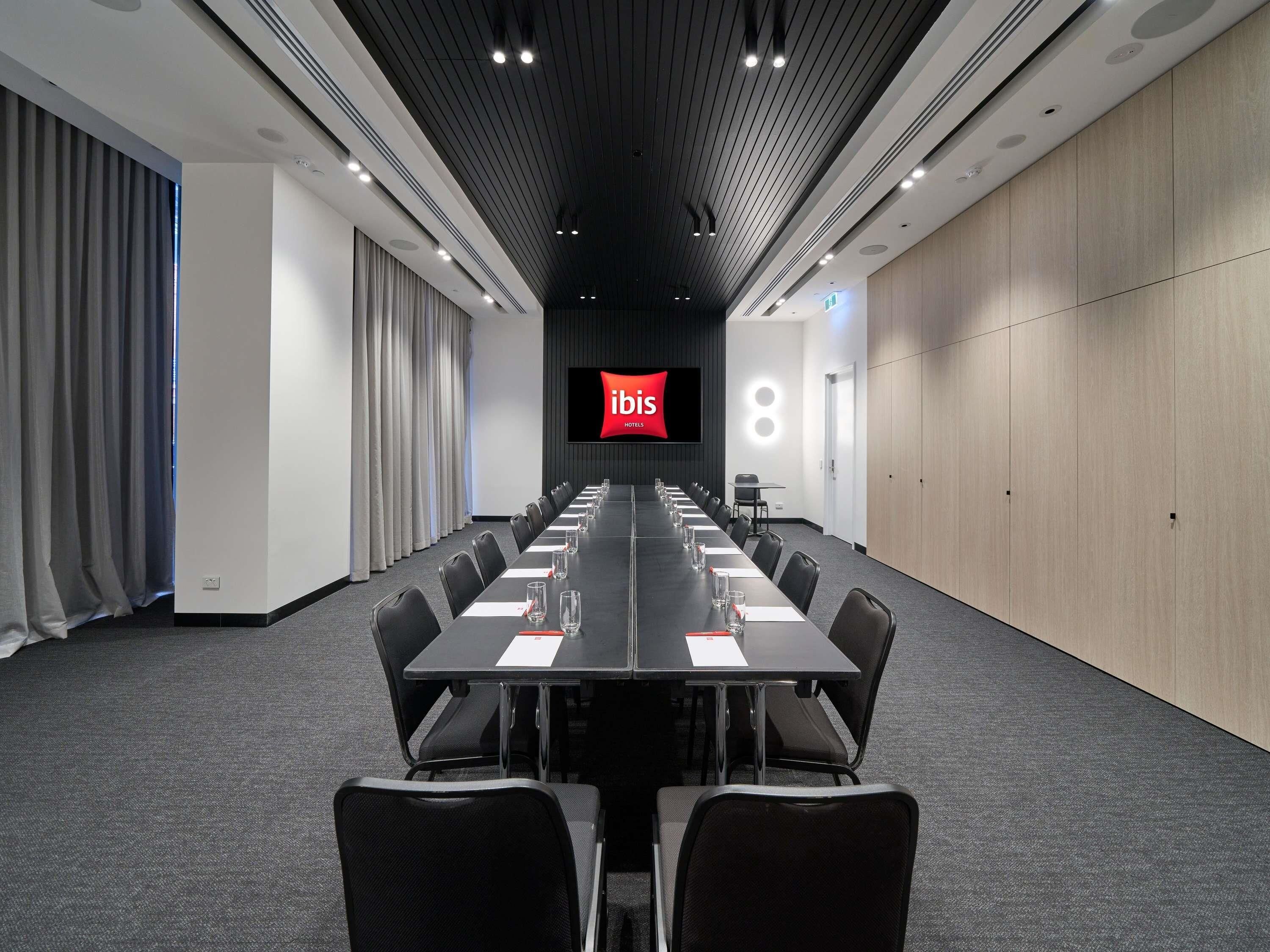 A conference room with a long table, chairs, a TV screen, and a wooden wall.