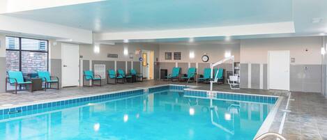 A swimming pool with blue tiles, surrounded by teal chairs and a tiled floor.