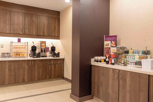 A kitchen area with wooden cabinets, a coffee machine, and various food items on the counter.