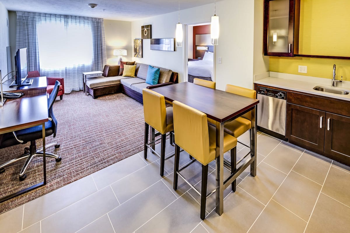 A hotel room with a dining area, a sofa, a TV, and a kitchen.