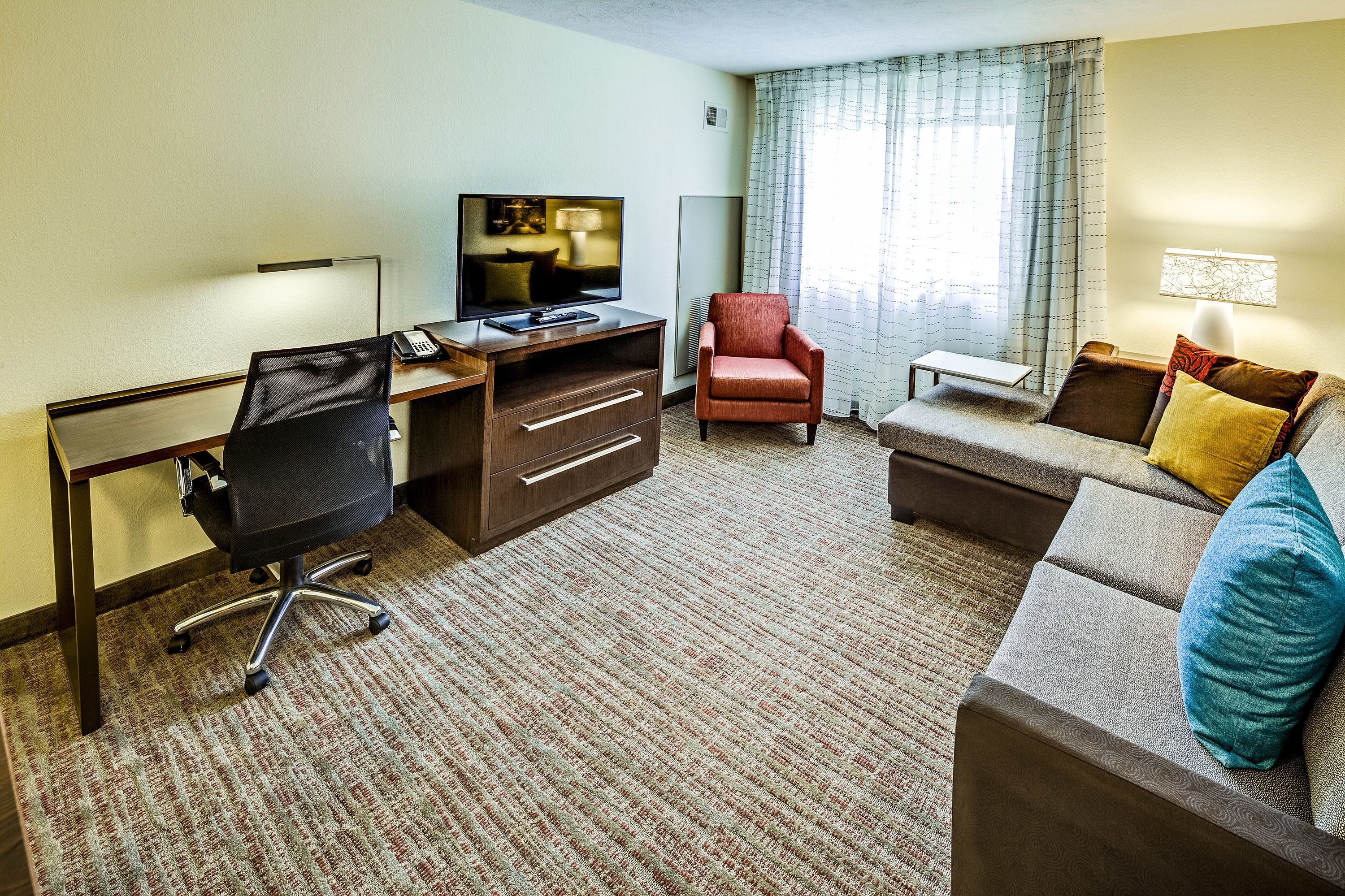 A hotel room with a desk, chair, sofa, and a television.