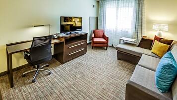 A hotel room with a desk, chair, sofa, and a television.