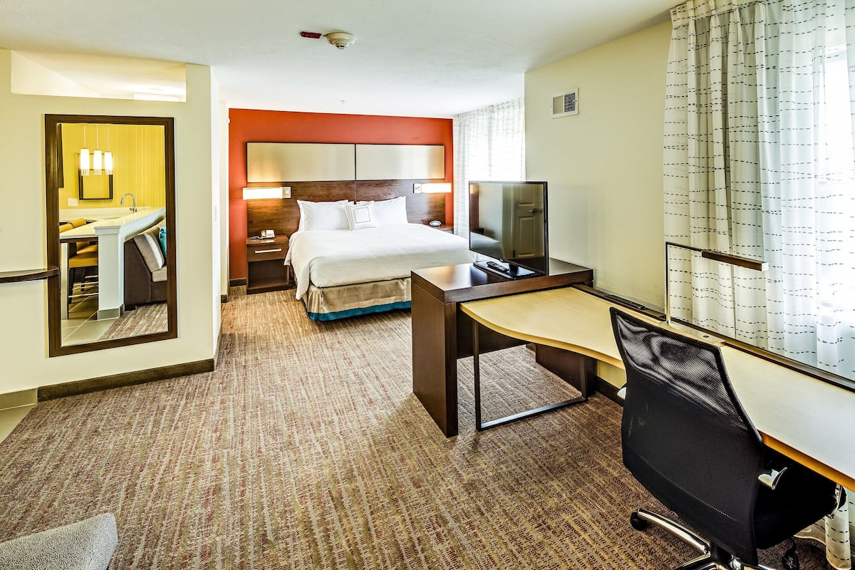 A hotel room with a bed, desk, chair, TV, and a bathroom with a mirror and sink.