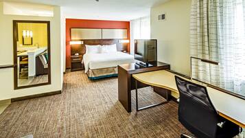 A hotel room with a bed, desk, chair, TV, and a bathroom with a mirror and sink.