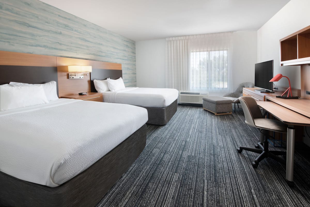 Ein Hotelzimmer mit zwei Betten, einem Schreibtisch, einem Stuhl, einem Fernseher und einem Fenster mit Vorhängen.