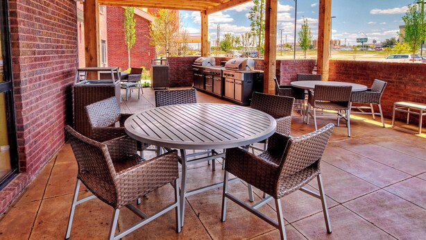 An outdoor patio with a brick wall, wicker furniture, a grill, and a view of the city.