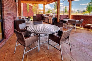 An outdoor patio with a brick wall, wicker furniture, a grill, and a view of the city.