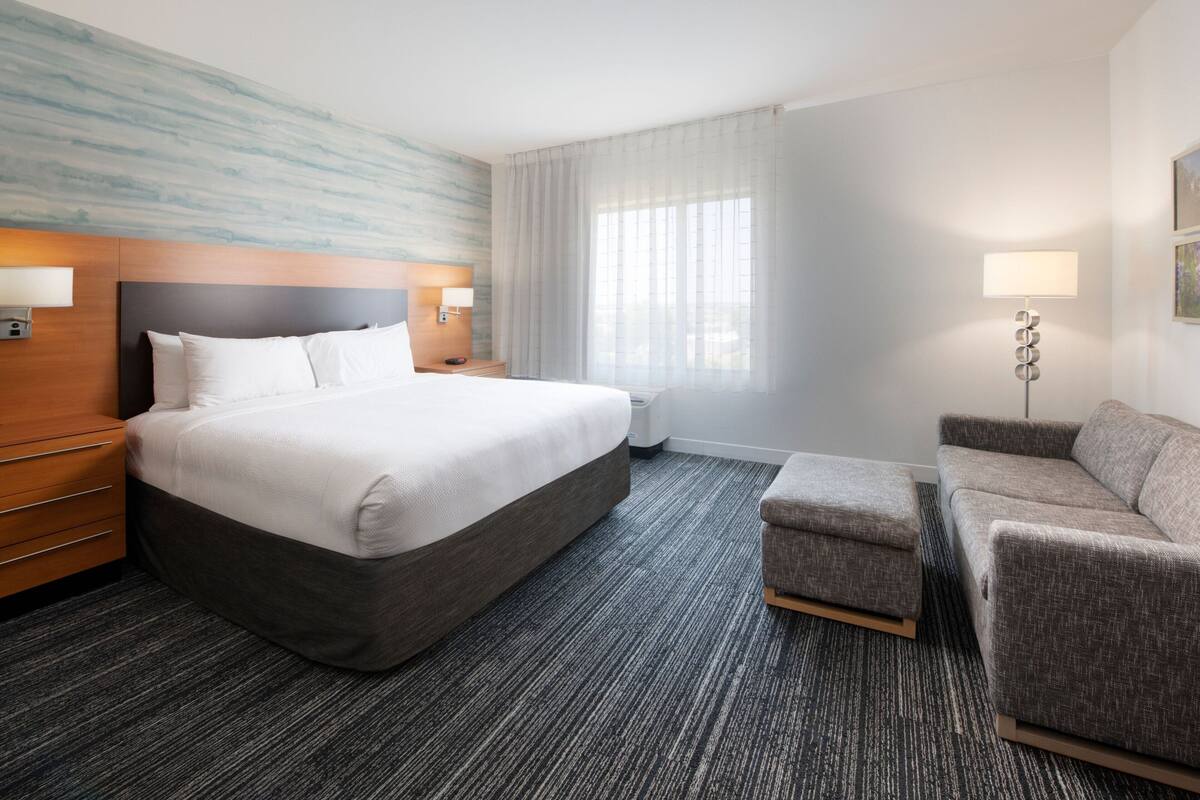Ein Hotelzimmer mit einem großen Bett, einer Couch, einem Nachttisch, einer Lampe und einem Wandbild.