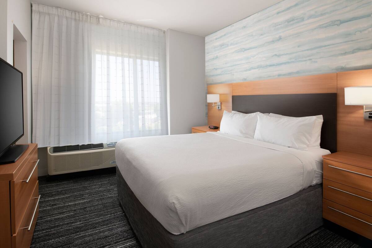 Ein Hotelzimmer mit einem großen Bett, einem Flachbildfernseher, einer Heizung, einem Nachttisch mit Lampe und einem Wandbild.
