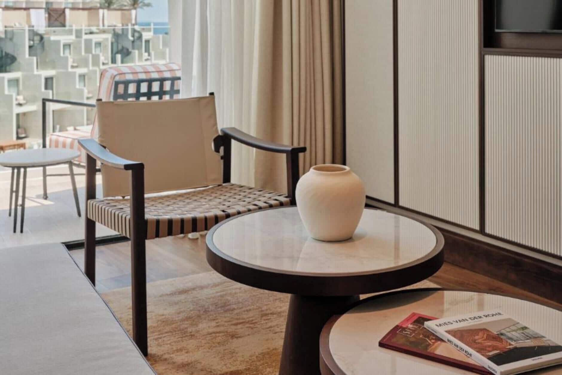 A hotel room with a round table, a chair, a vase, and a magazine on the table.
