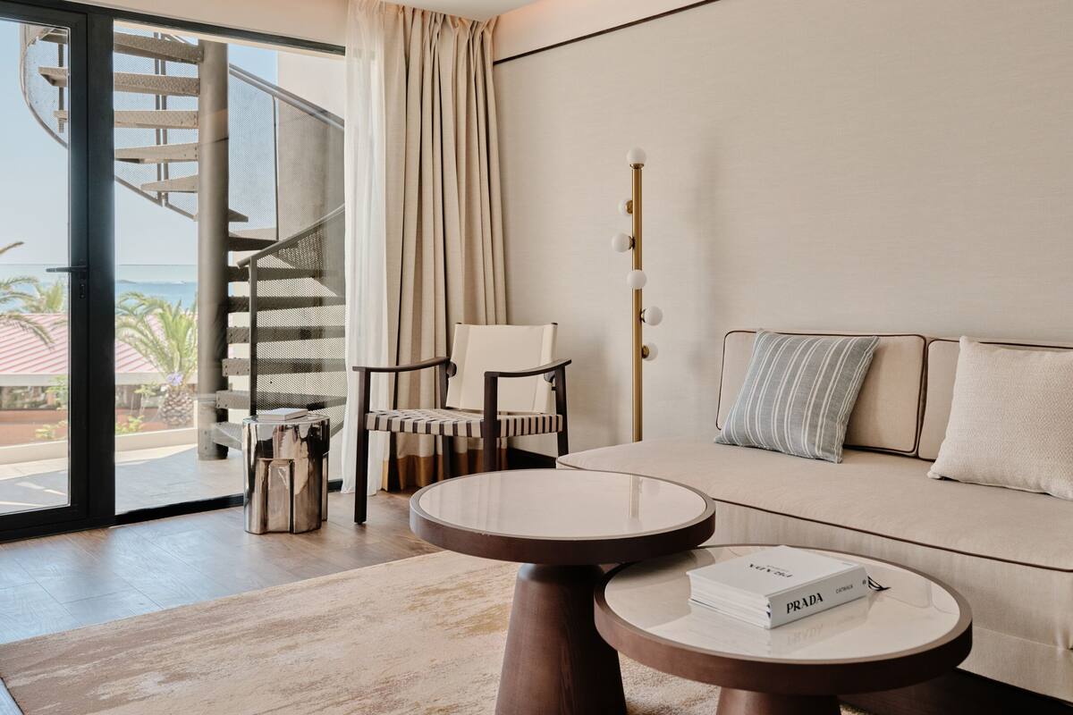 Ein modernes Wohnzimmer mit einer Couch, einem runden Tisch, einem Sessel, einer Treppe und Blick ins Freie.