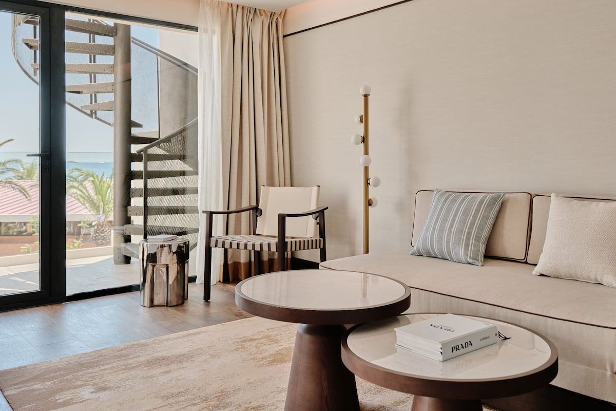 A modern living room with a sofa, a round table, a chair, a staircase, and a view of the outdoors.