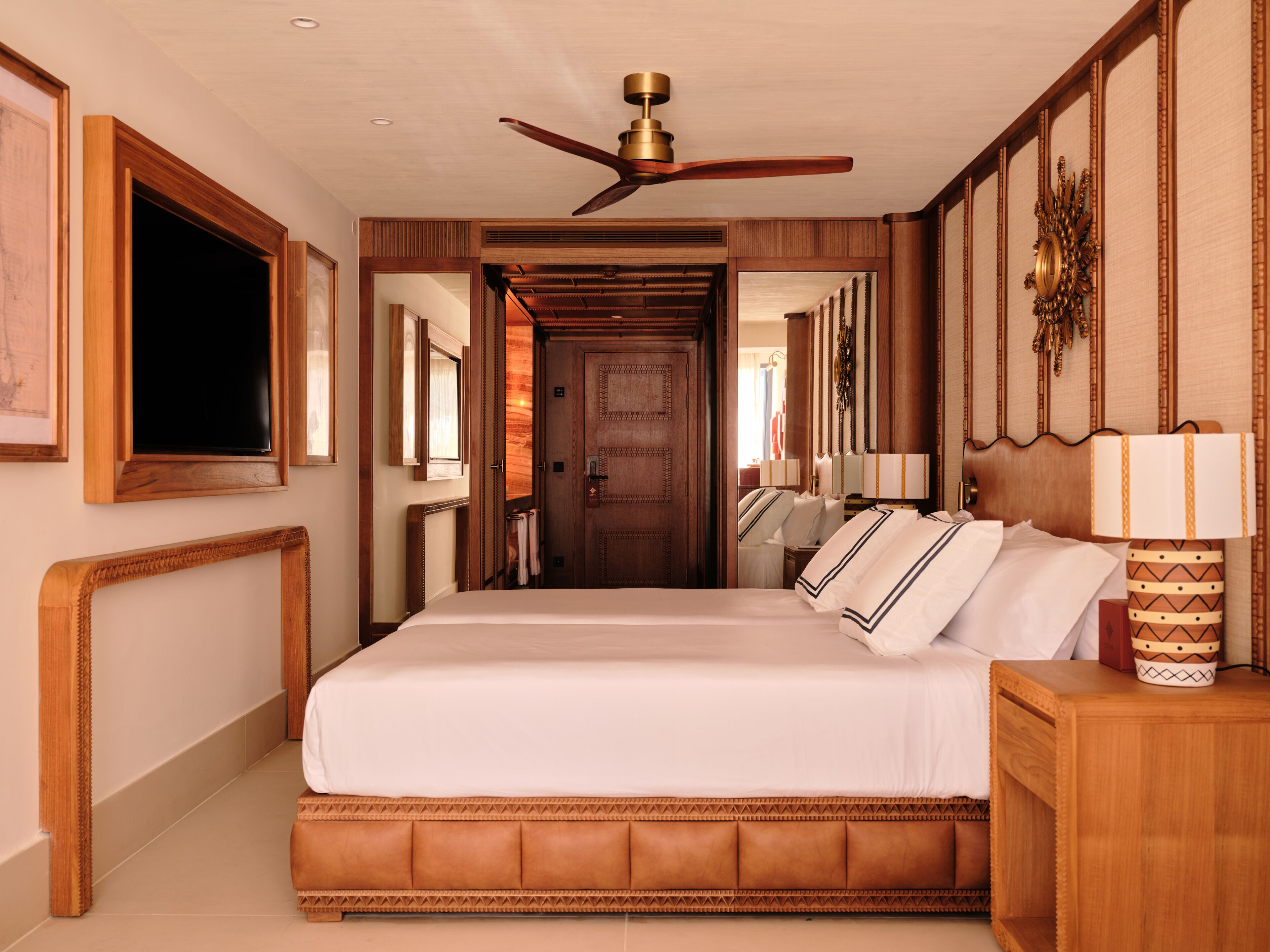 A hotel room with a large bed, a ceiling fan, a wooden door, and a mirror on the wall.