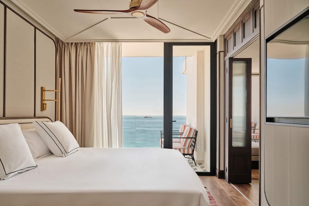 Ein Hotelzimmer mit einem großen Bett, einem Deckenventilator, Meerblick und einem Balkon mit einem Stuhl.