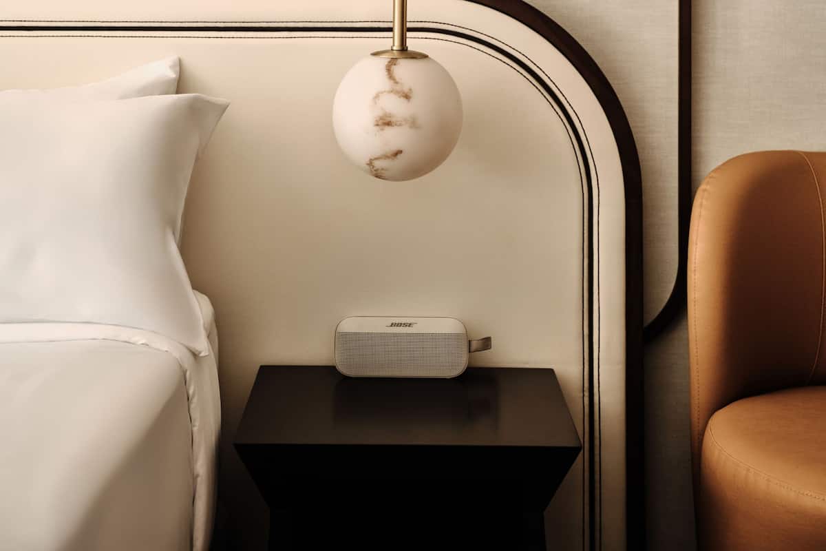 A modern hotel room with a bed, a small bedside table, a lamp, and a chair.