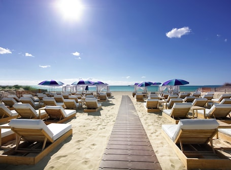 On the beach, sun-loungers, beach umbrellas, beach bar. BLESS Ibiza The Site - New Opening 2026
