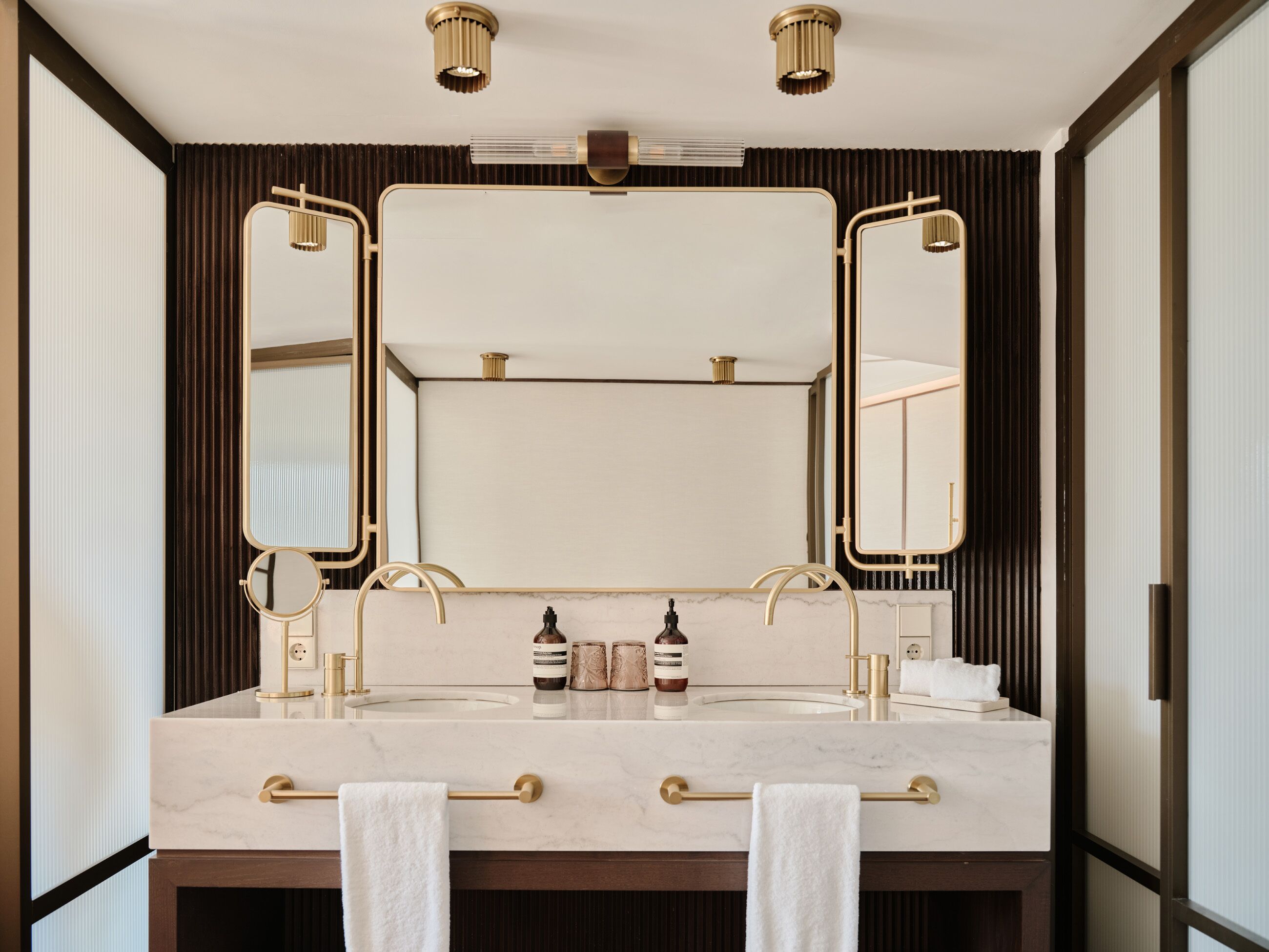A bathroom with a double sink, two mirrors, a towel rack, and a large mirror above the sink.