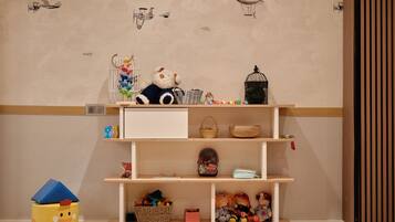 Ein Zimmer mit Holzboden, einem weißen Regal mit Körben und Spielzeug, und einer Wand mit Flugzeugmotiven.