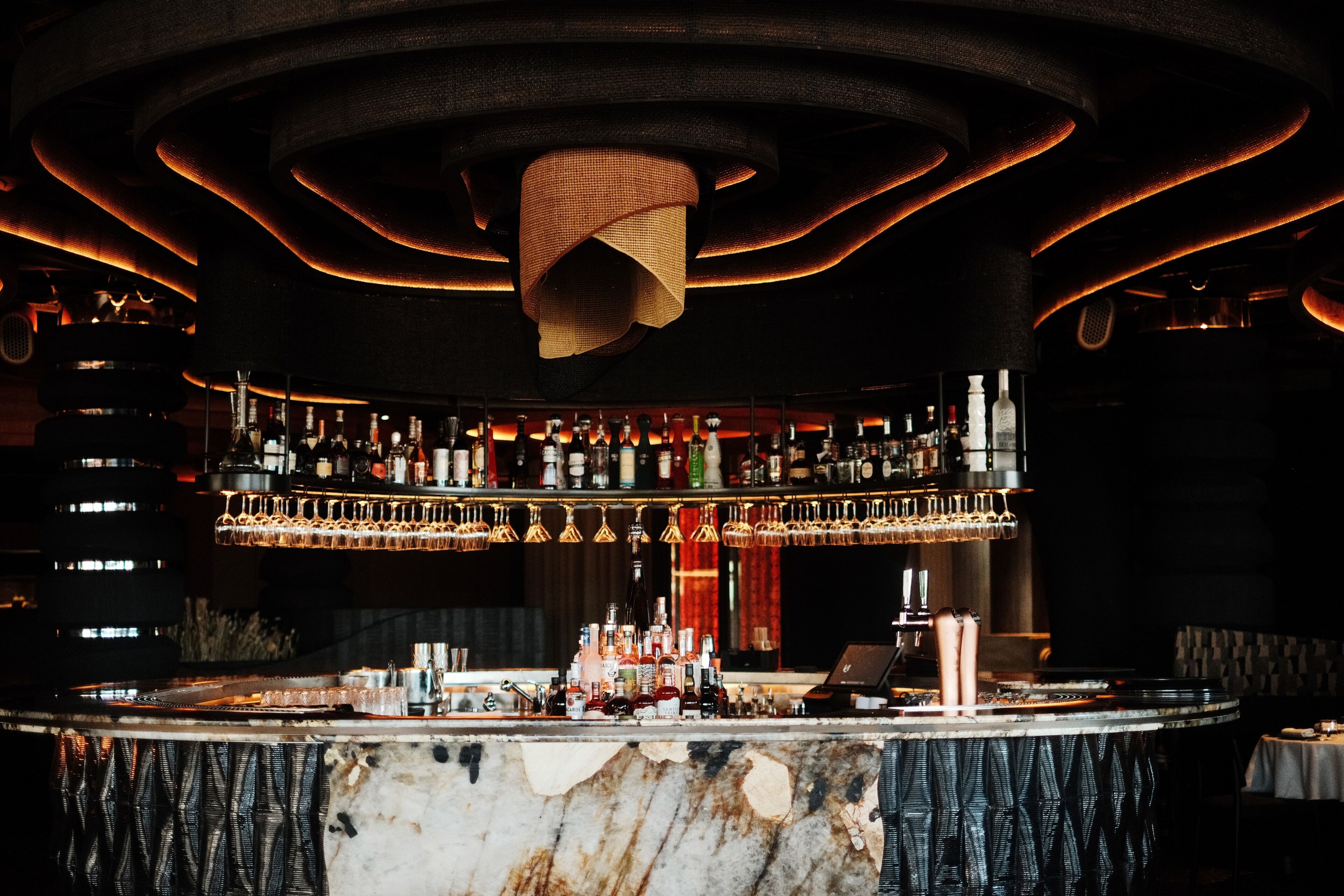 A bar area with a circular bar counter, multiple shelves of bottles, and a unique hanging light fixture.
