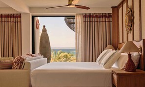 A hotel room with a bed, a nightstand, a lamp, a ceiling fan, and a view of the ocean. - BLESS Ibiza The Site - New Opening 2026 (Sant Josep de sa Talaia)