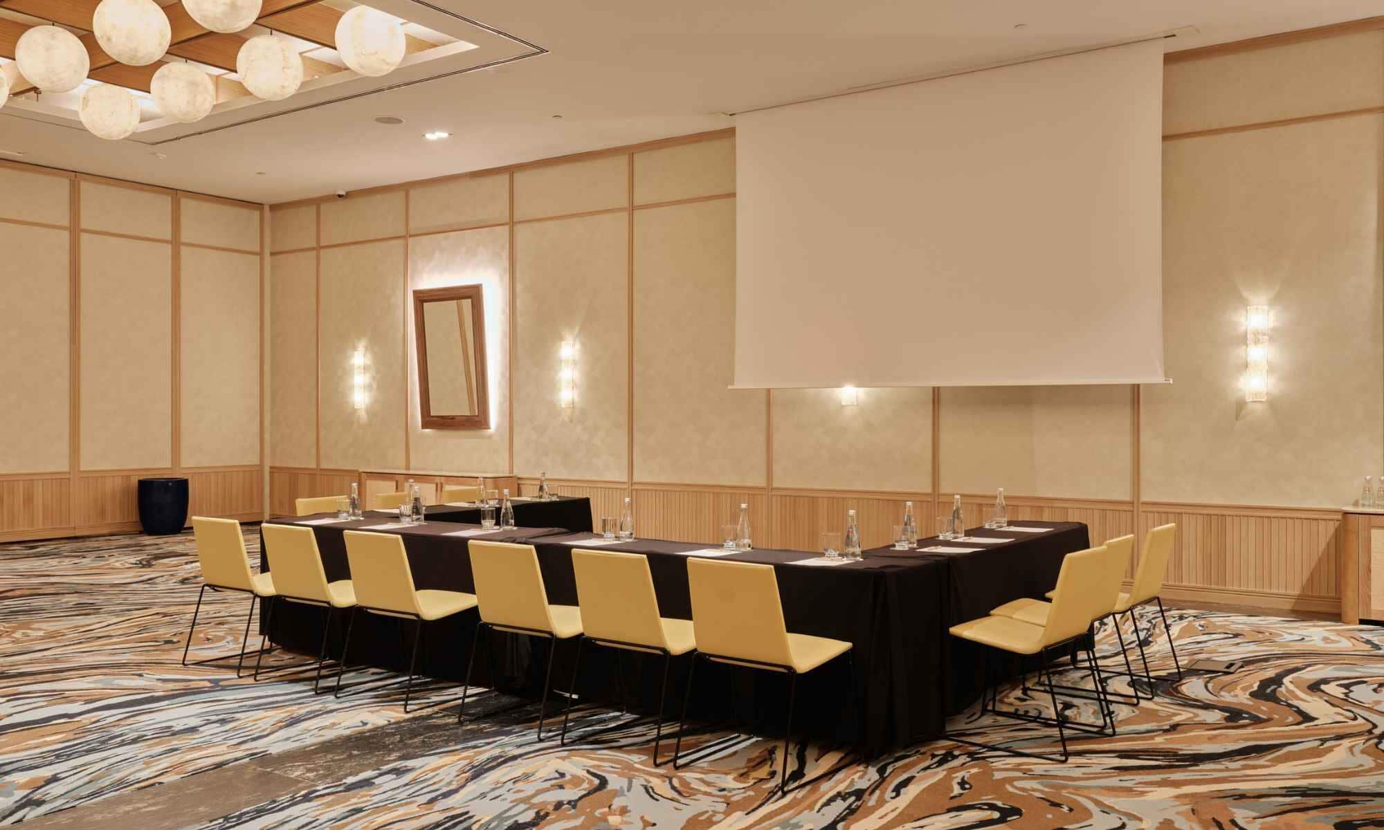 Une salle de conférence équipée d’une longue table, de chaises, d’un écran de projection et d’un grand miroir.