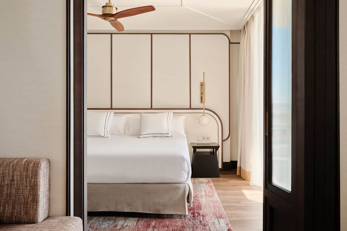 Ein modernes Hotelzimmer mit Bett, Nachttisch, Deckenventilator und Blick durch ein Fenster.