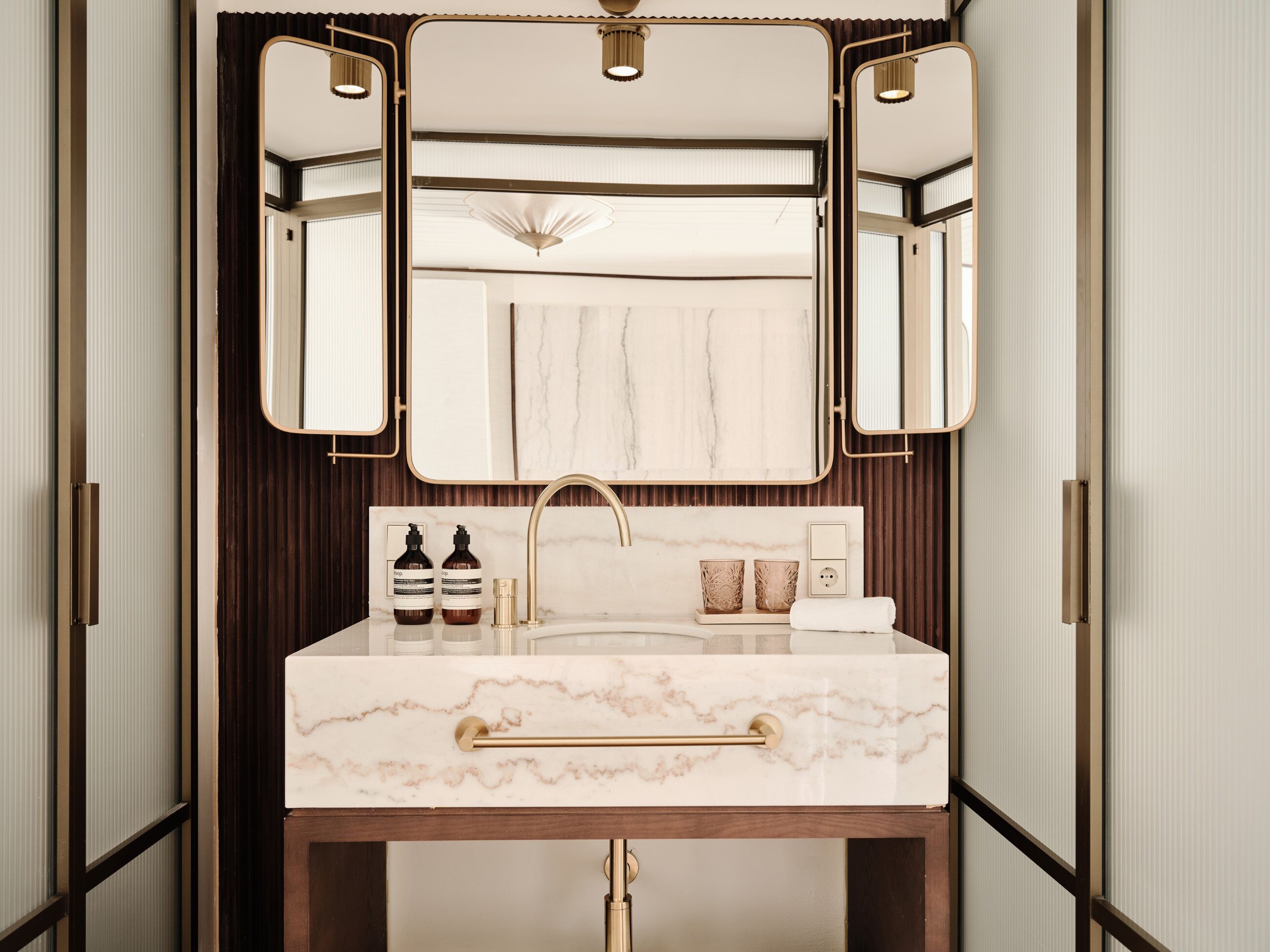 A bathroom with a marble sink, gold fixtures, and a large mirror.