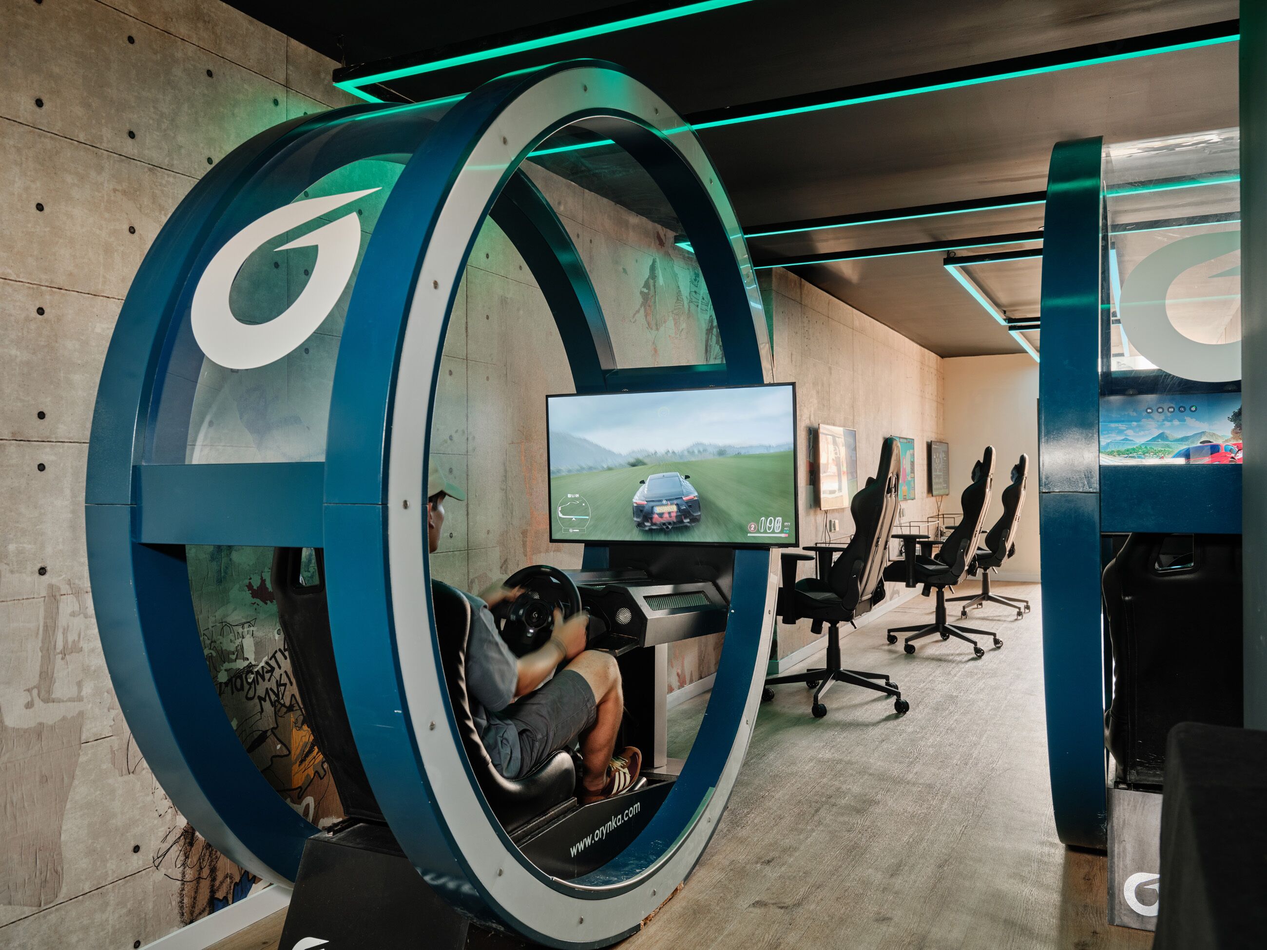 Et rum med en stor, rund konstruktion, et ophængt skærm og flere gamingstole.