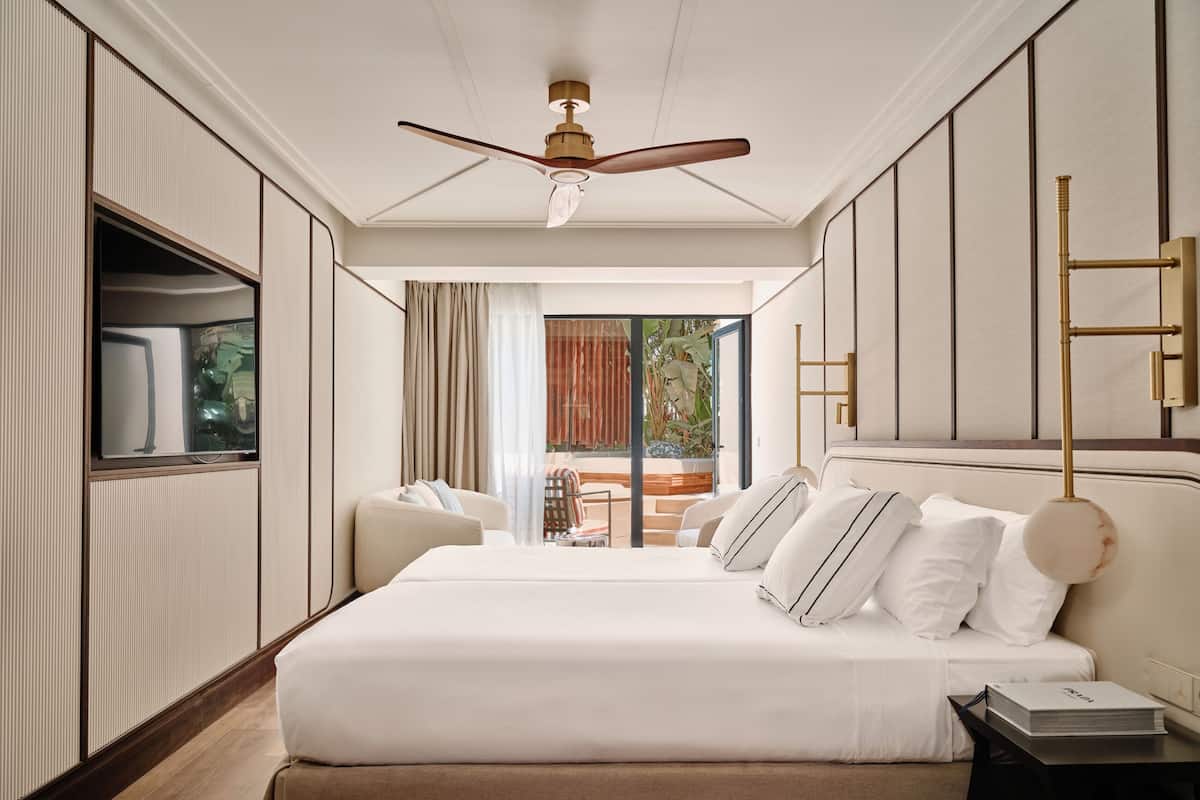 Ein Hotelzimmer mit Bett, Deckenventilator, Fernseher, Nachttisch und Blick ins Freie.