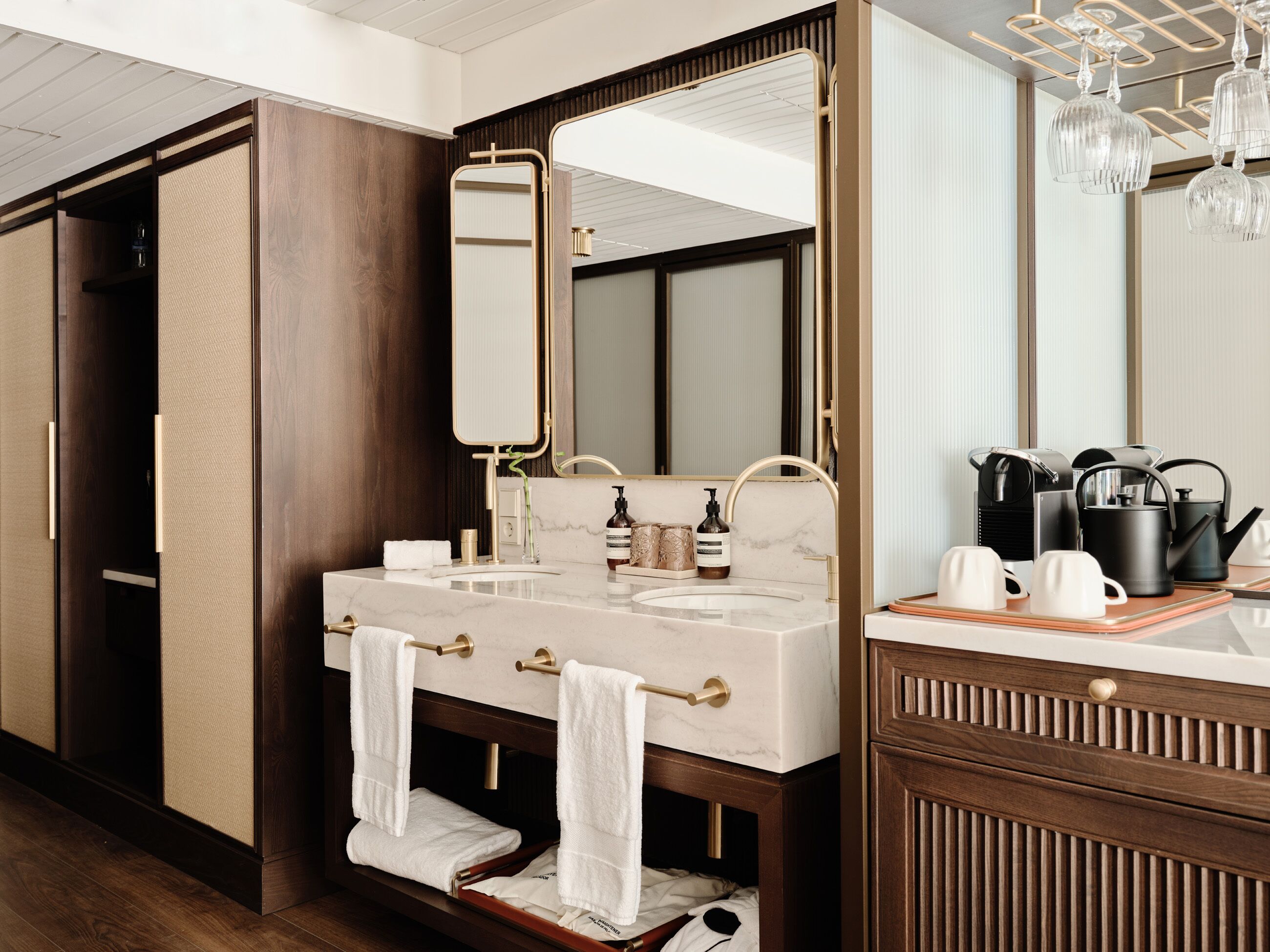 A bathroom with a large mirror, two sinks, a towel rack, and a coffee station.