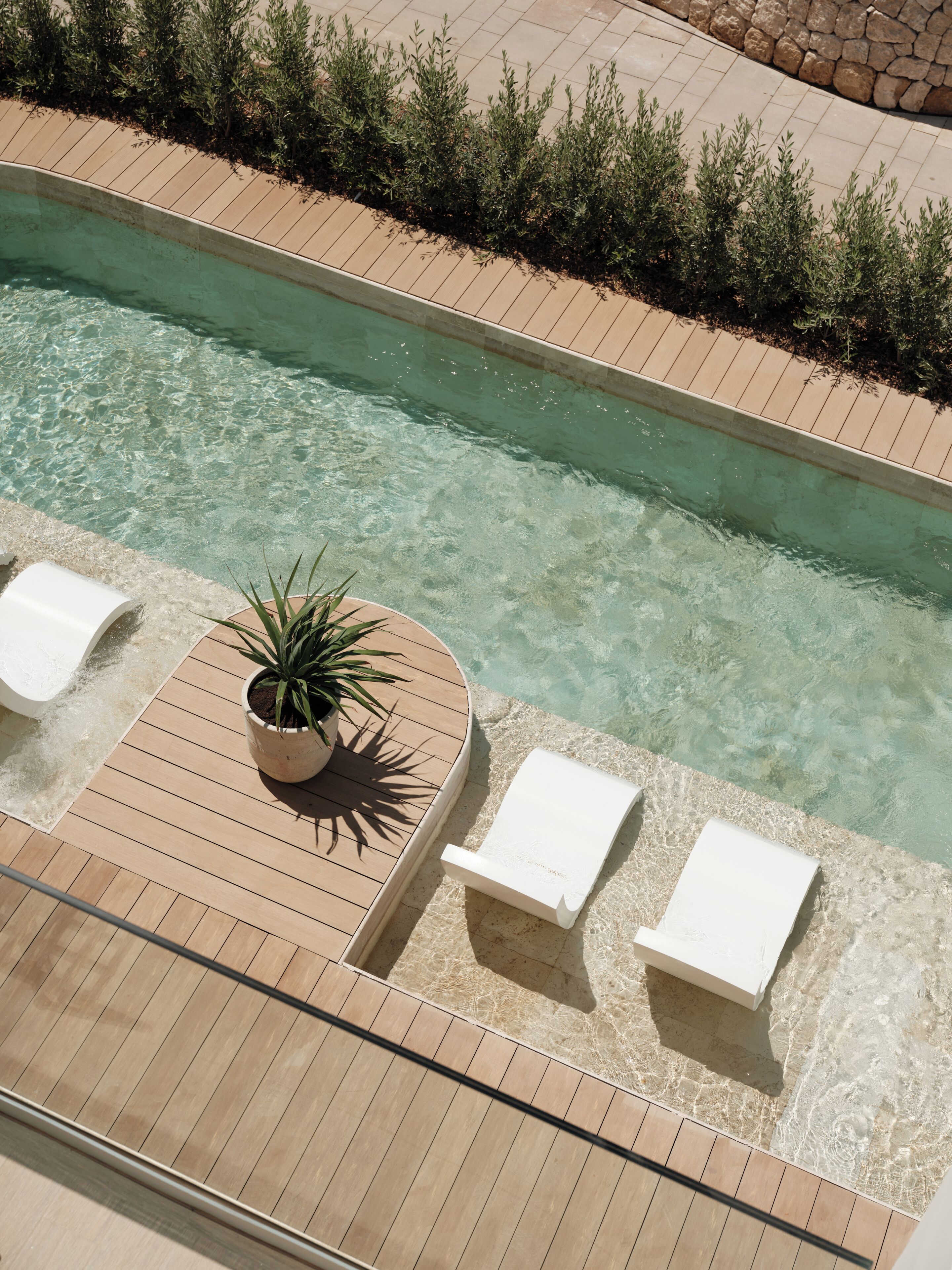 A pool with clear water, surrounded by a wooden deck and potted plants.
