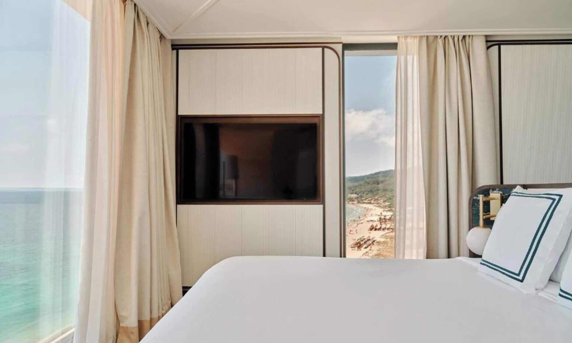 Una habitación de hotel con una cama grande, una ventana que da a la playa y cortinas.