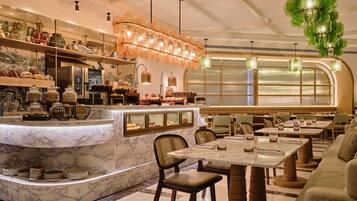 Ein Restaurantinneres mit Marmorarbeitsplatten, Glaskühlvitrinen und einer Sitzgegend mit Tischen und Stühlen.