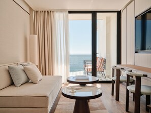 Quarto de hotel com sofá, mesa redonda, cadeira e vista para o mar.