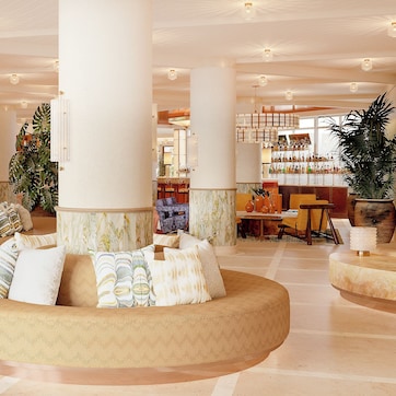 A spacious lobby with a central seating area, large columns, and a bar in the background.
